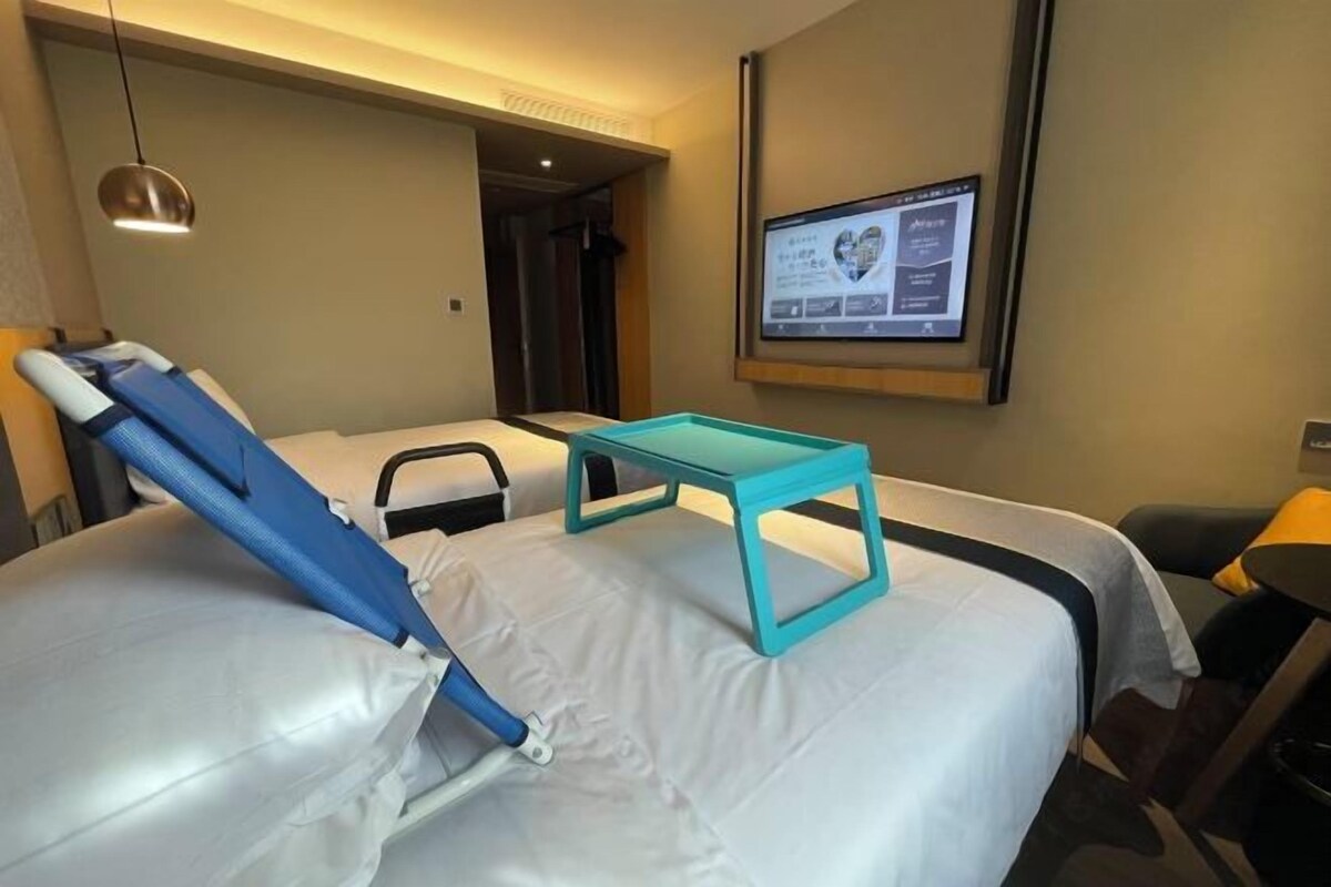 A hotel room with a massage chair, a small table, and a screen displaying a heart rate monitor.