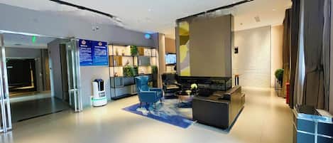 A modern hotel lobby with a reception desk, seating area, and a large screen.