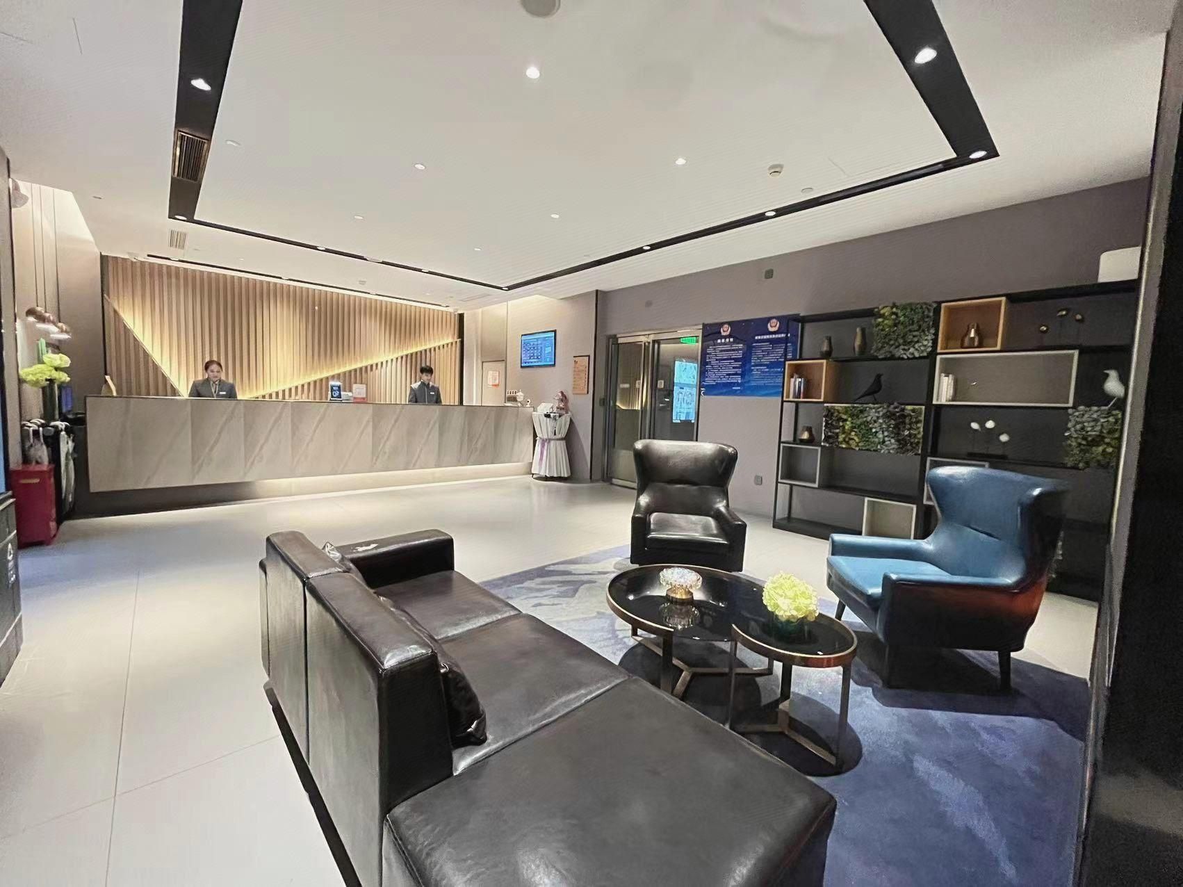 A modern hotel lobby with a reception desk, seating area, and a wall with informational displays.
