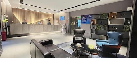 A modern hotel lobby with a reception desk, seating area, and a wall with informational displays.