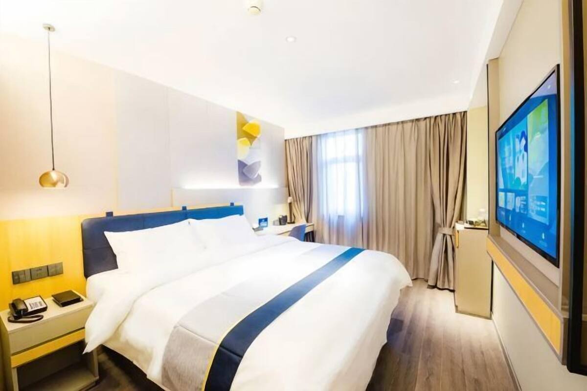 Une chambre d’hôtel avec un grand lit, une table de chevet, une lampe, une télévision et des rideaux.