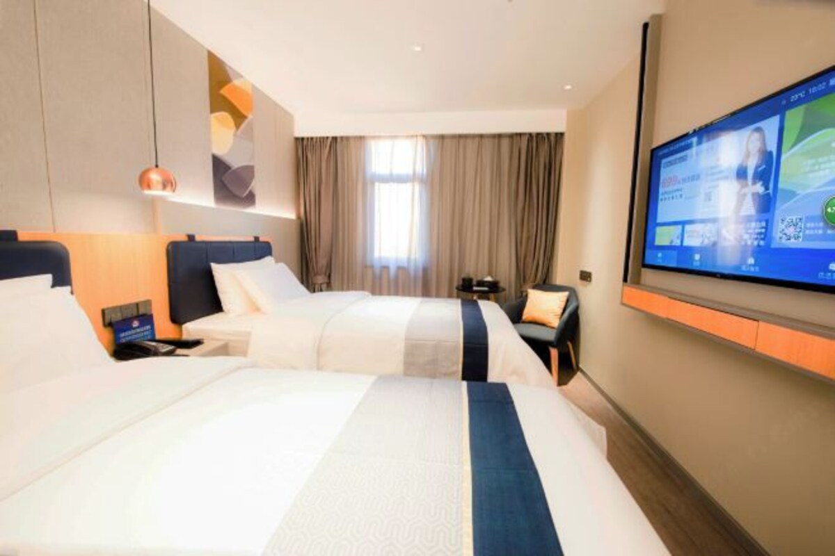 A hotel room with two beds, a TV on the wall, and a large window with curtains.