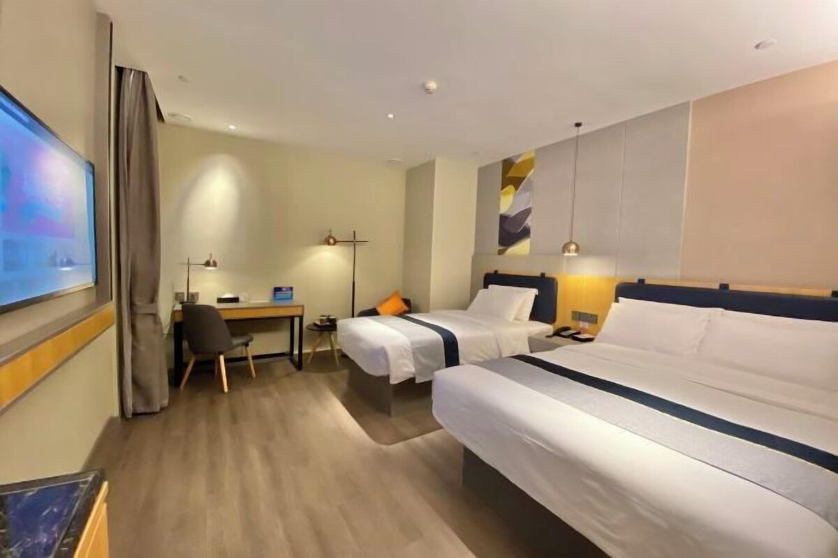 A hotel room with two beds, a desk, a chair, a TV, and a lamp.