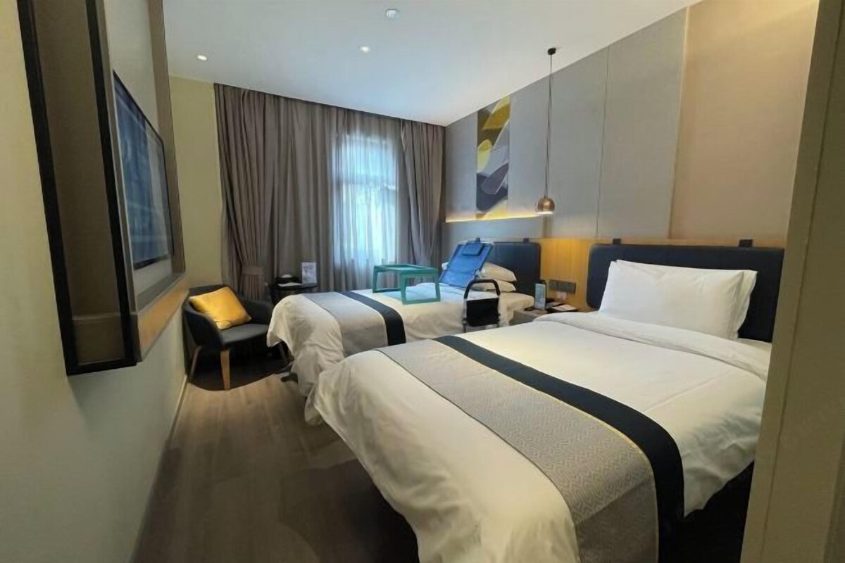 A hotel room with two beds, a desk, a chair, a small table, and a window with curtains.