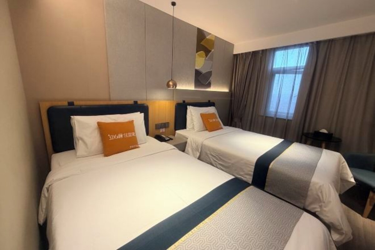 A hotel room with two beds, each with a pillow and a bedside table.