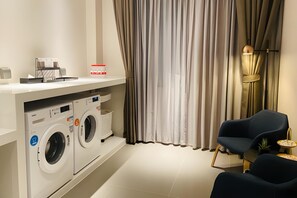 Une buanderie moderne équipée de deux machines à laver à chargement frontal, d’une petite table avec une lampe et d’une chaise.