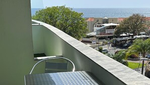 A balcony with a table and chairs, a view of the sea, and a building in the background. - Lido Branca by Olá Madeira (Funchal)
