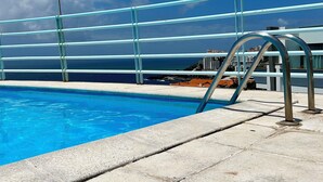 A swimming pool with a metal railing and a view of the ocean and buildings in the background. - Lido Branca by Olá Madeira (Funchal)