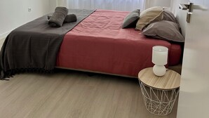 A bedroom with a bed, a bedside table, a lamp, and a window with sheer curtains. - Lido Branca by Olá Madeira (Funchal)