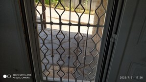 Uitzicht door een metalen hek met een geometrisch patroon, op een geplaveid gebied met planten en een muur.