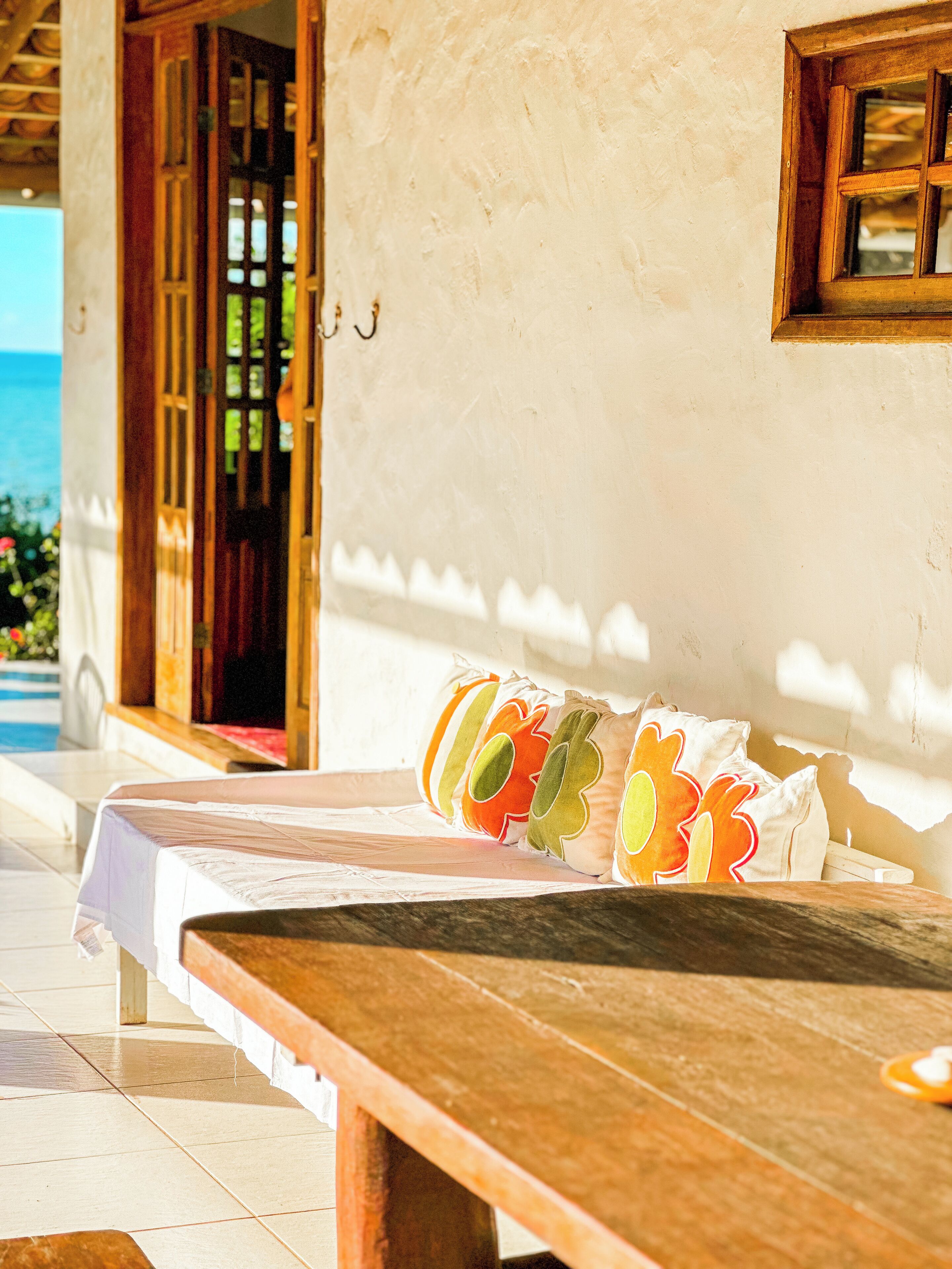A wooden bench with colorful pillows, a wooden door, and a view of the ocean.
