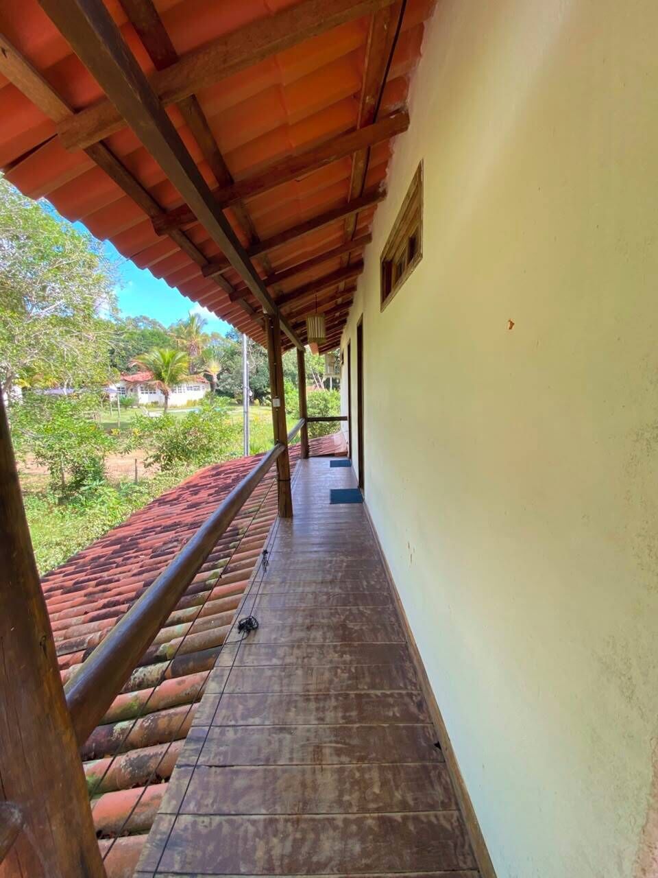 Un pasillo cubierto con suelo de baldosas, vigas de madera y vistas al exterior con vegetación.
