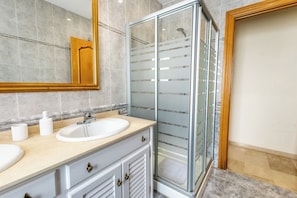 A bathroom with a glass shower enclosure, a sink with a vanity, and a mirror.