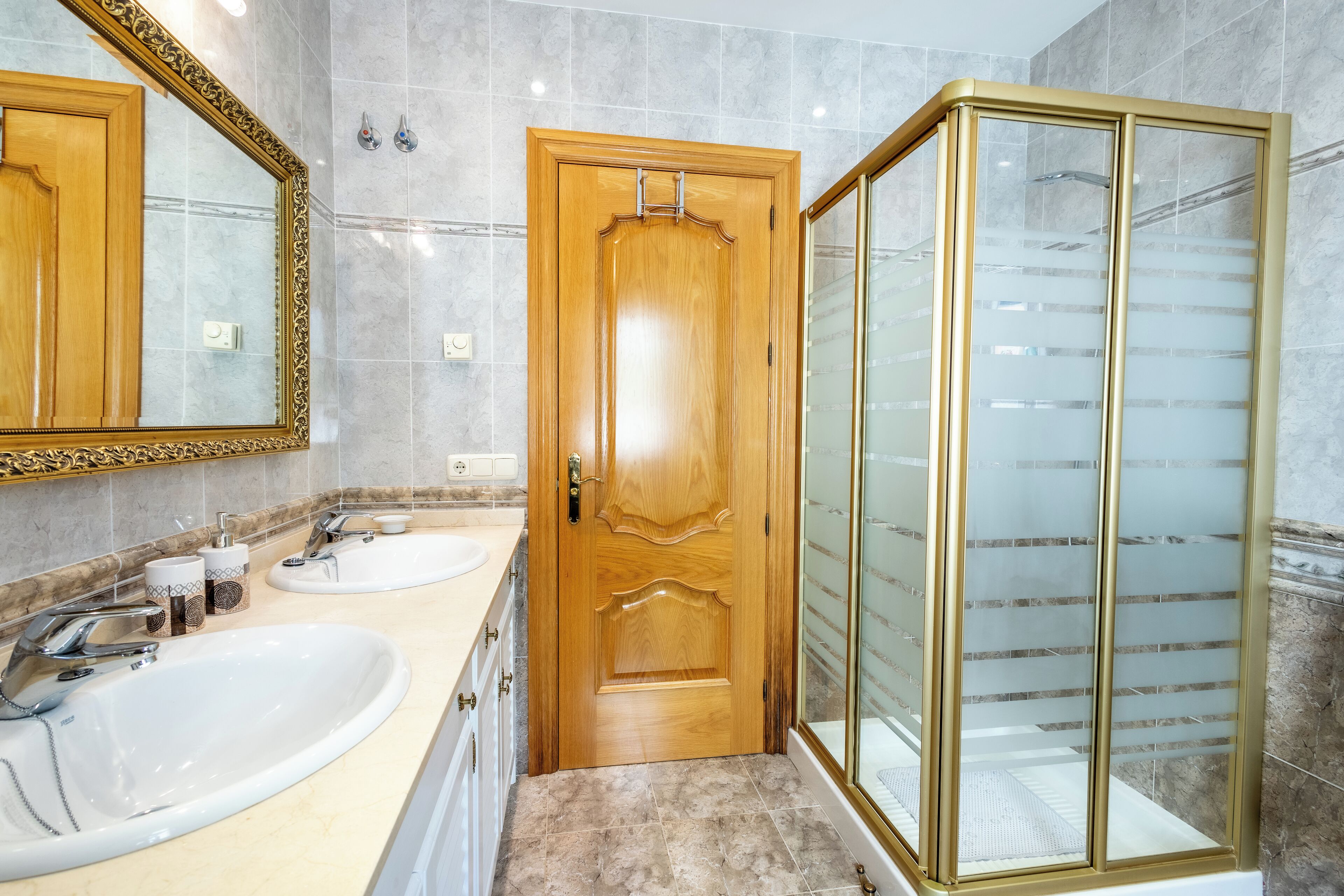 A bathroom with two sinks, a wooden door, and a glass shower enclosure.