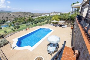 A swimming pool with a patio area, including lounge chairs and a table with umbrellas. - Stunning Golf Villa With Pool and Stunning Views (Alhaurin el Grande)