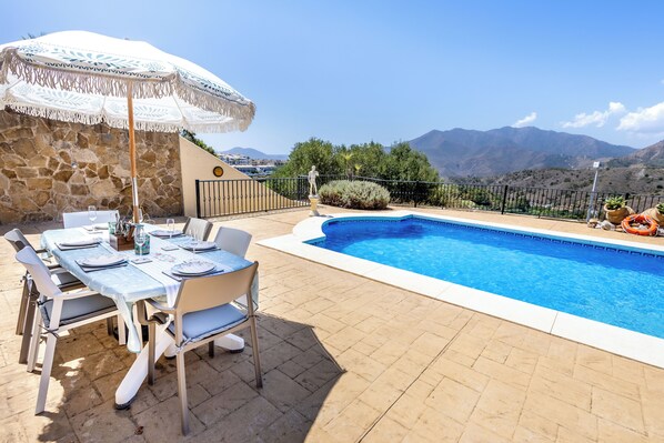 A poolside area with a table set for dining, a decorative umbrella, and a view of mountains. - Stunning Golf Villa With Pool and Stunning Views (Alhaurin el Grande)