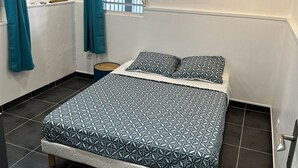 A bedroom with a bed, curtains, an air conditioning unit, a window with bars, and a wall-mounted artwork. - Bienvenue au Chacha (FORT-DE-FRANCE)