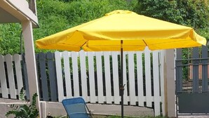 A yellow umbrella, a blue and yellow folding chair, and a white picket fence in a garden area. - Bienvenue au Chacha (FORT-DE-FRANCE)