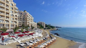 Ein Strandhotel mit mehreren Balkonen, Liegestühlen und Sonnenschirmen direkt am Ufer.