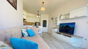 Ein modernes Wohnzimmer mit einem beigefarbenen Sofa, blauen Kissen, einem Flachbildfernseher und einem Holztisch.