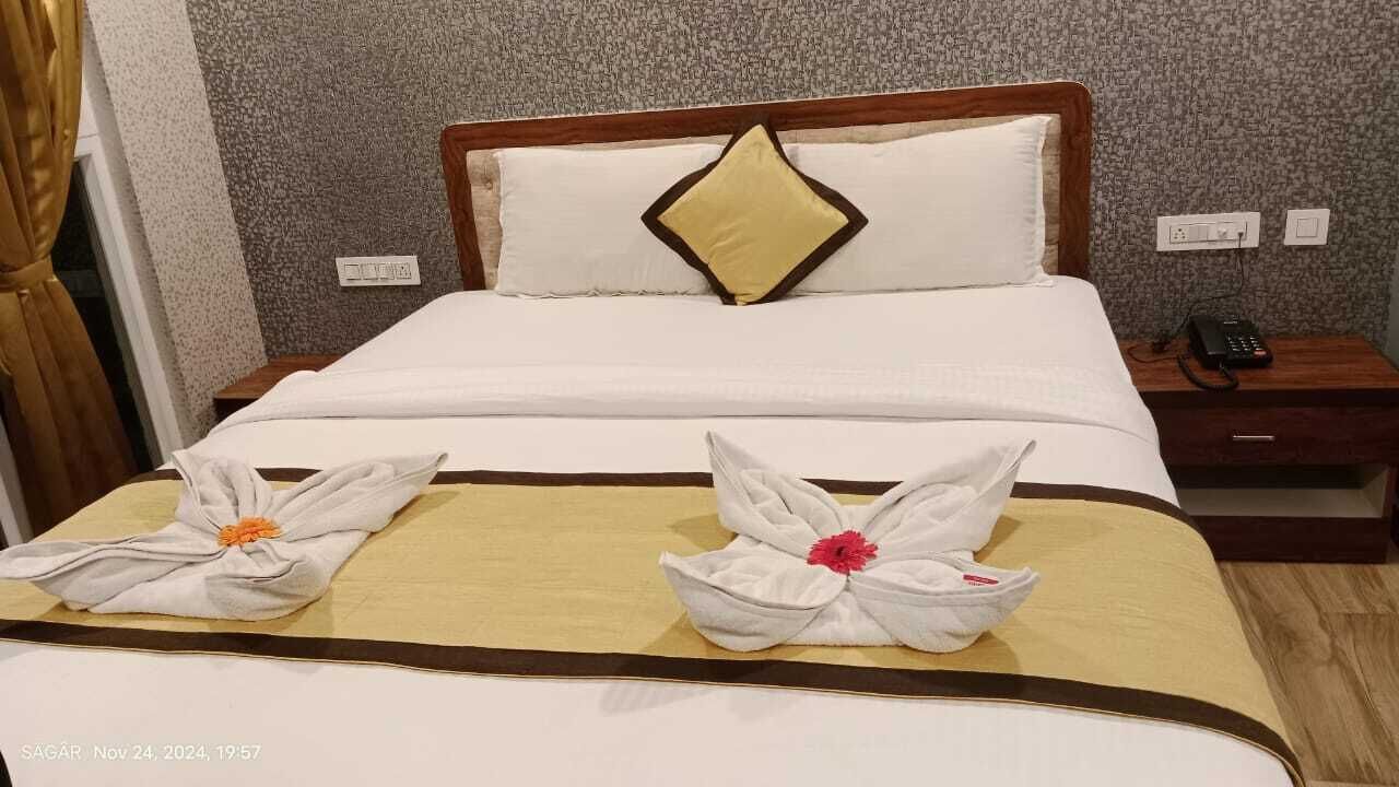 Una habitación de hotel con una cama bien hecha, un cabecero de madera, una mesita de noche con teléfono y una pared con papel tapiz texturizado.