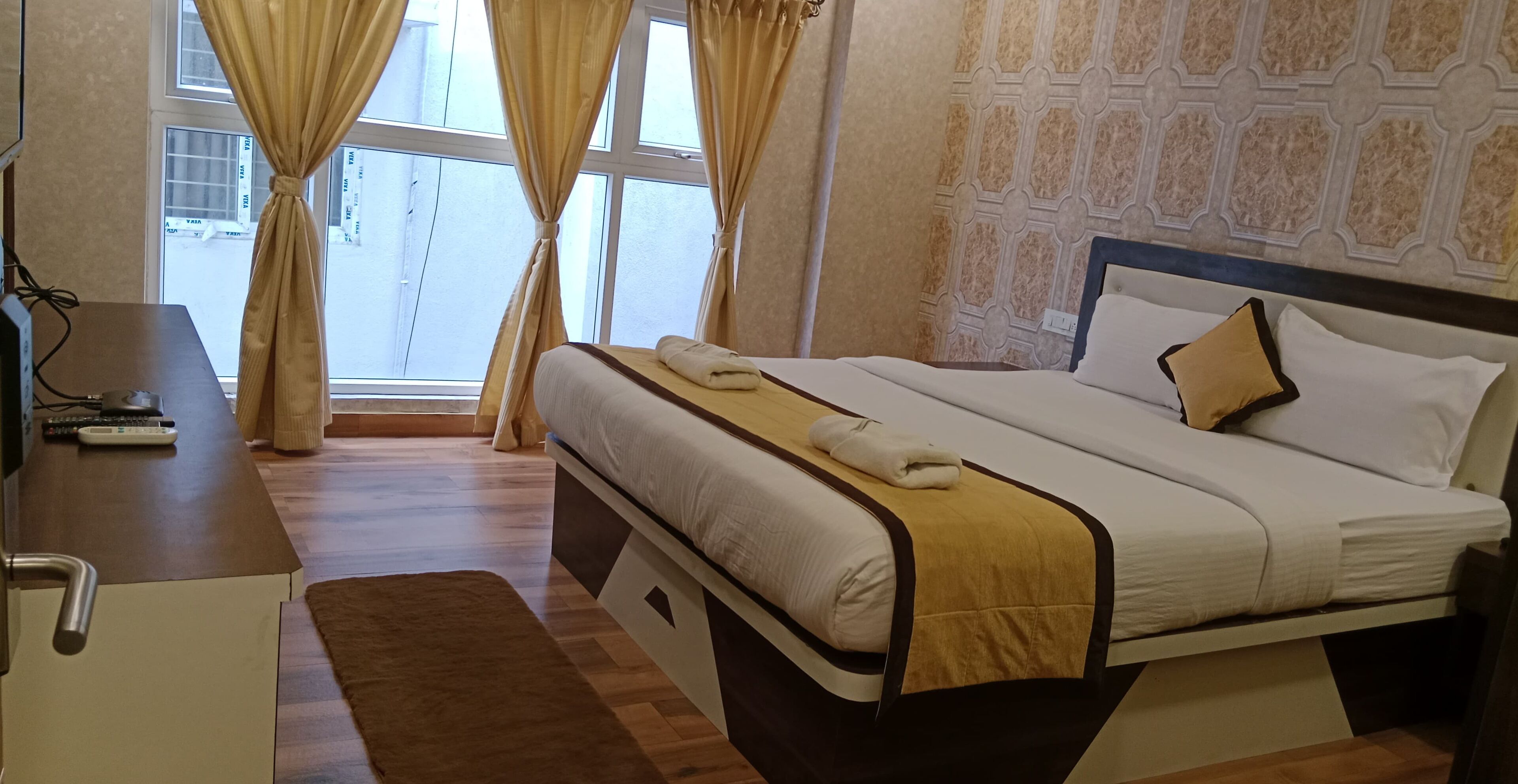 Una habitación de hotel con una cama, un escritorio con computadora y un ventanal con cortinas.