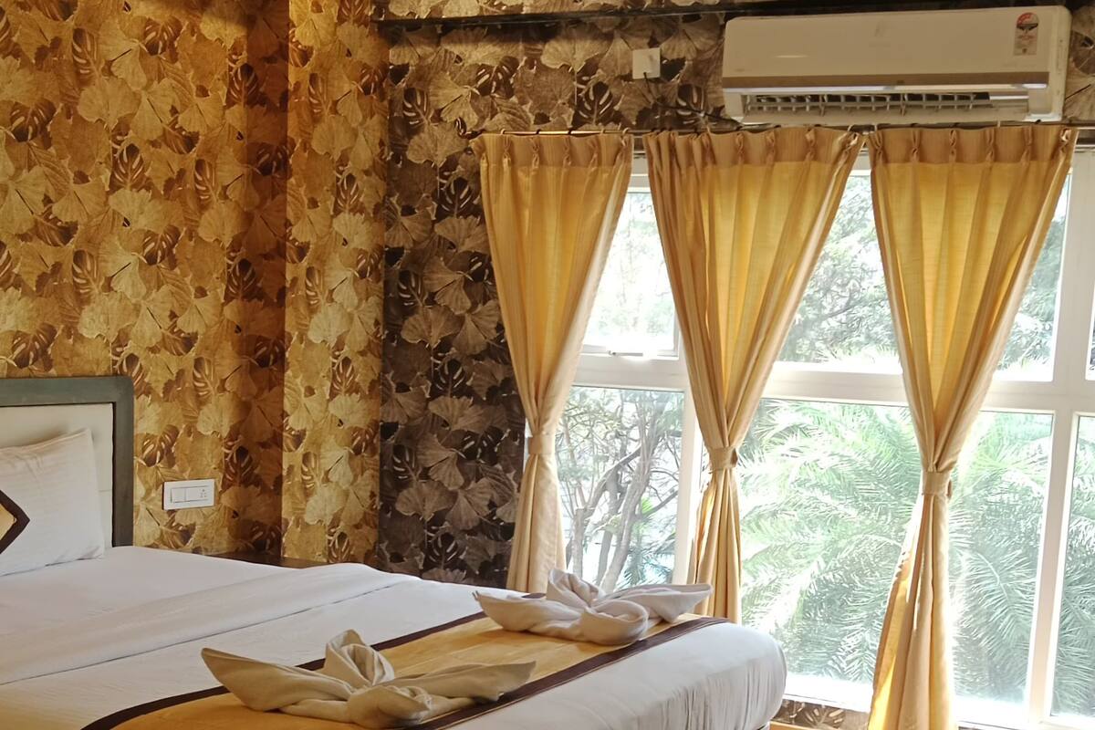 Ein Hotelzimmer mit Bett, Deckenventilator, Klimaanlage und Blick auf Bäume durch das Fenster.