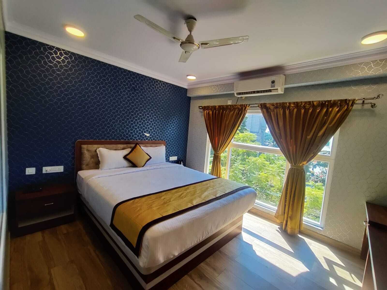 A hotel room with a large bed, a ceiling fan, an air conditioning unit, and a window with curtains.