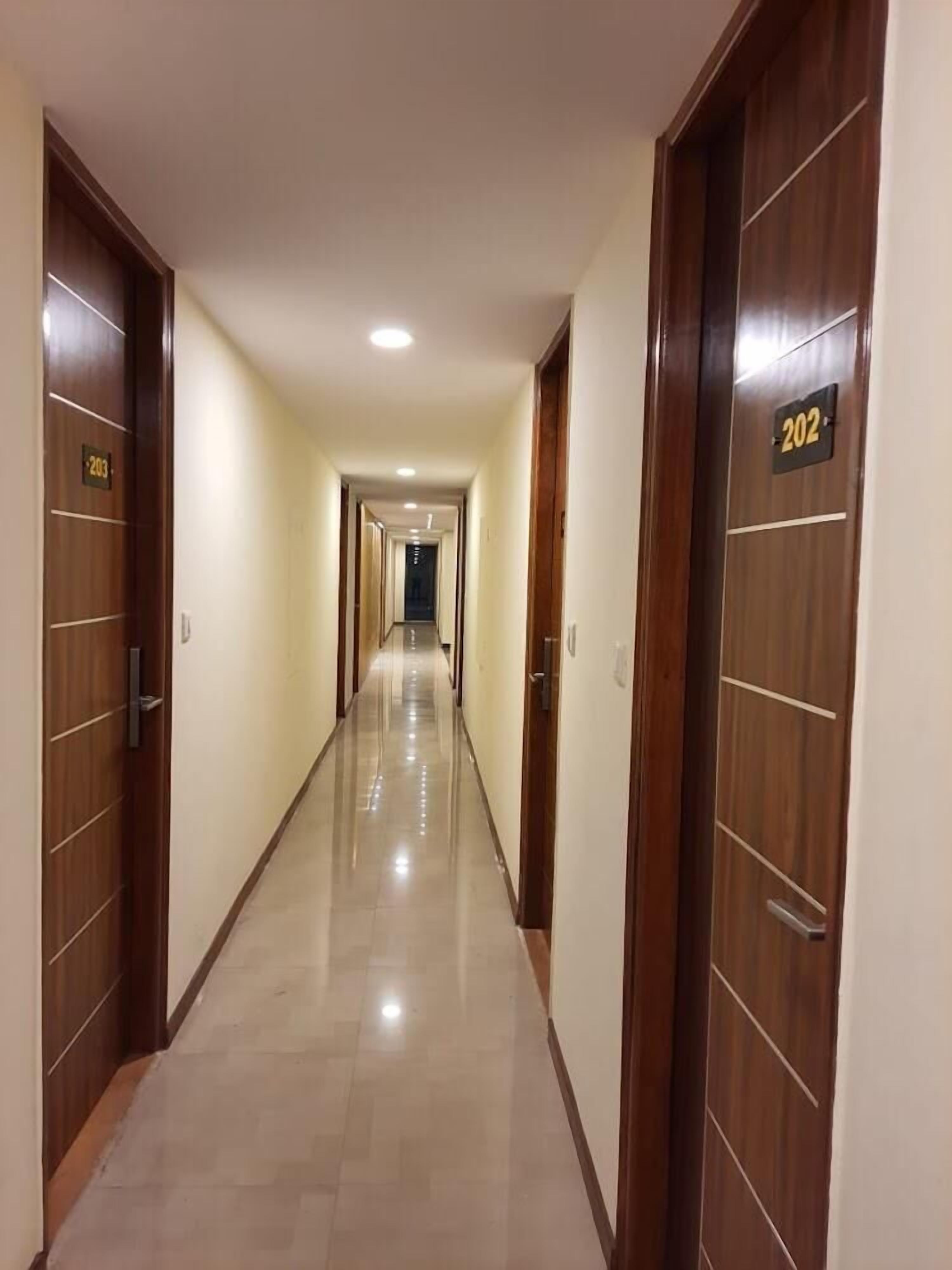 A hotel corridor with wooden doors, numbered room signs, and a tiled floor.