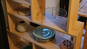 A wooden shelf unit with multiple compartments, including a spice rack, a small vase, and stacked plates. - Mersea Island Retreat - 4 Bedroom House (Colchester)