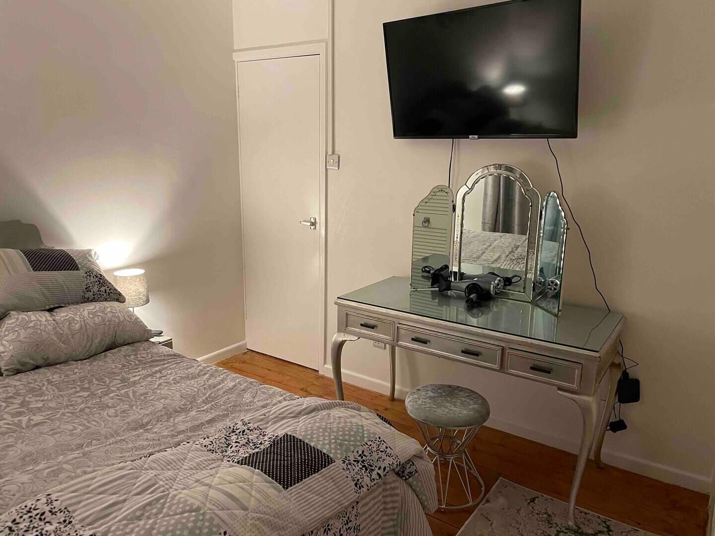 A bedroom with a bed, a dresser with a mirror, a television, and a lamp.