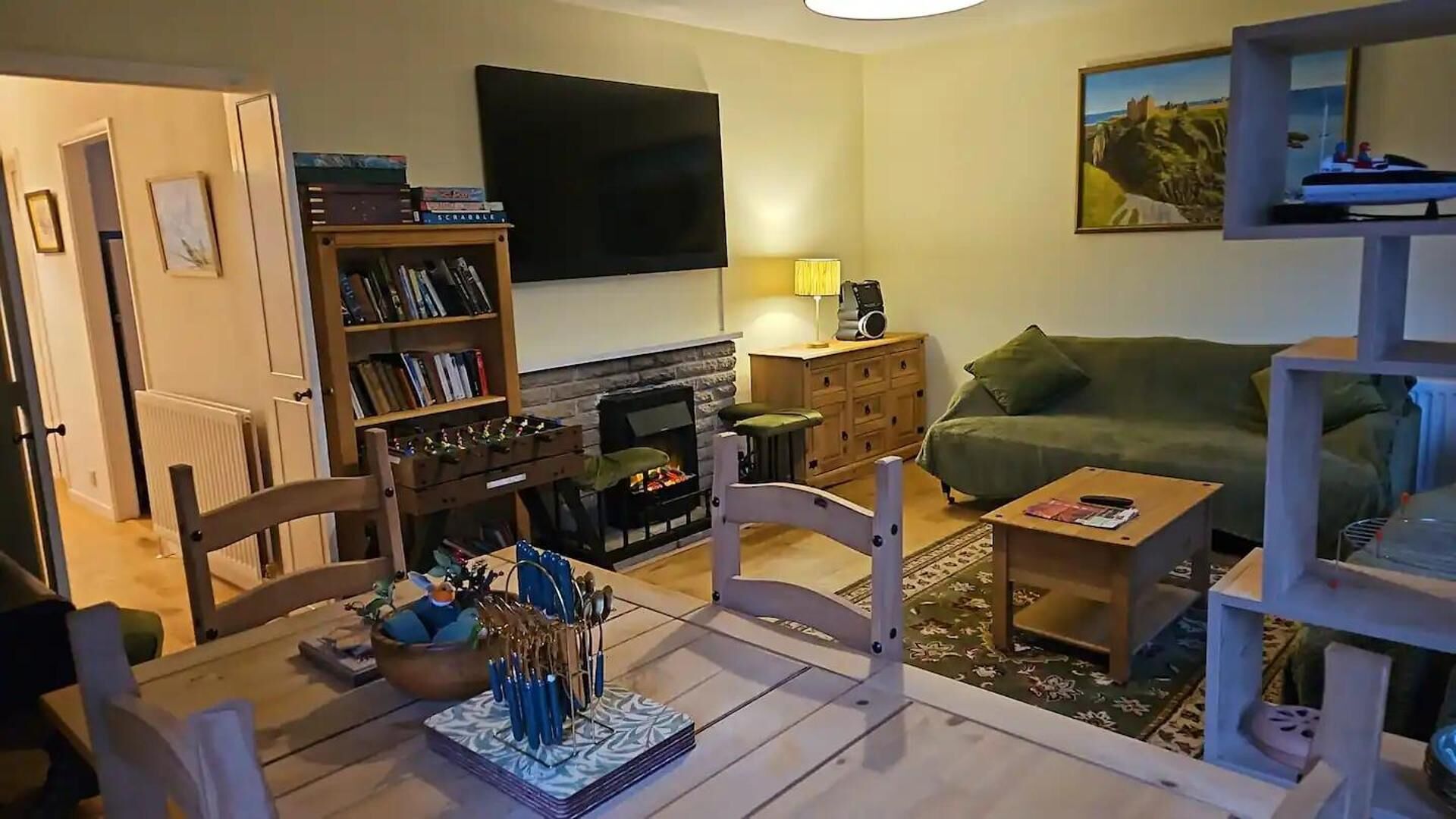 Een woonkamer met een open haard, een groene bank, een salontafel en een boekenkast.