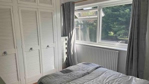 A bedroom with a bed, a window with curtains, and a white wardrobe. - Mersea Island Retreat - 4 Bedroom House (Colchester)