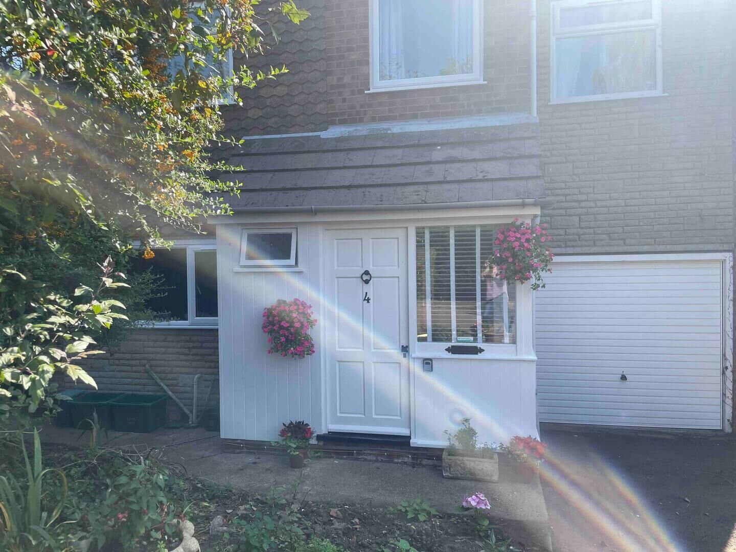 A residential house with a white front door, a small porch with a flower pot, and a garage door.