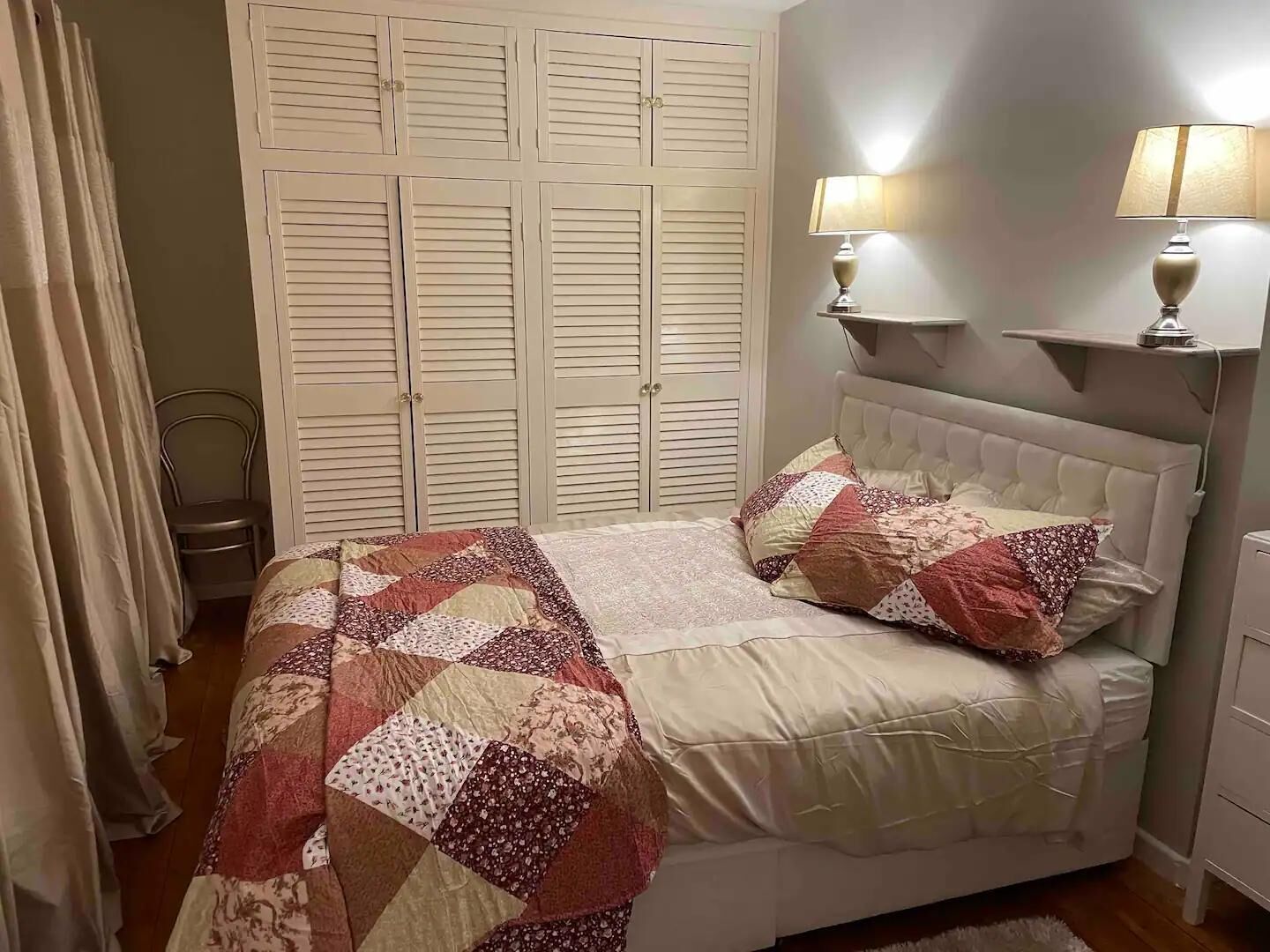 A bedroom with a bed, a nightstand, a lamp, and a wardrobe.