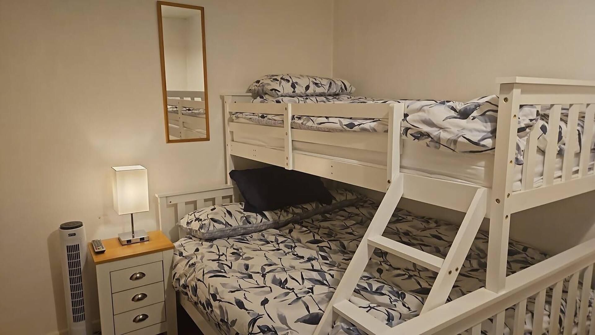A bunk bed room with a mirror, bedside table, and a lamp.
