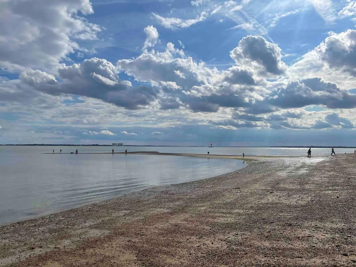 A beach with a wide expanse of water and a pebbly shore.