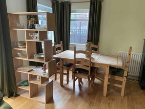 Un comedor con mesa y sillas de madera, una estantería empotrada con cristalería y vistas al exterior a través de una ventana con cortinas.