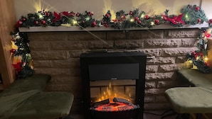 A fireplace with a stone wall backdrop, flanked by two green cushioned chairs. - Mersea Island Retreat - 4 Bedroom House (Colchester)
