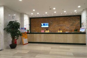 A reception desk with a television screen, a potted plant, and a signboard.
