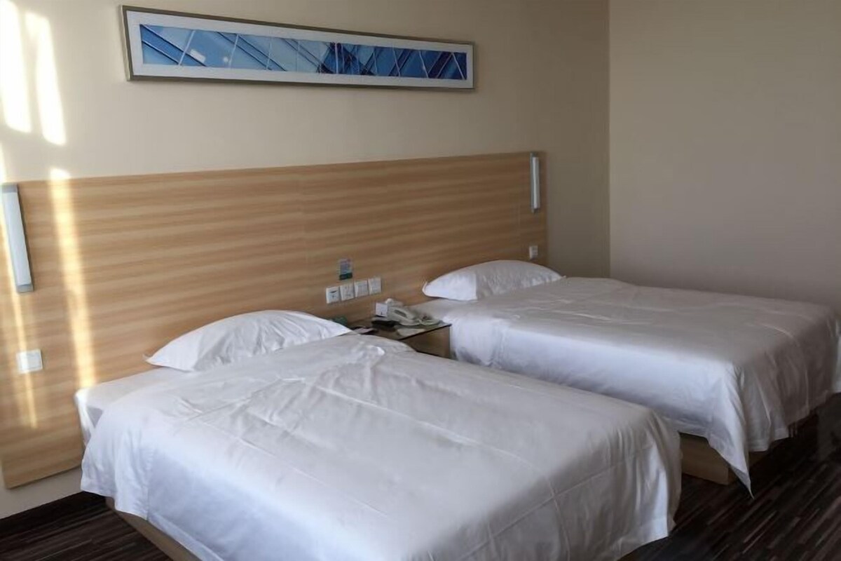 A hotel room with two beds, a wooden headboard, a bedside table with a phone, and a framed picture on the wall.