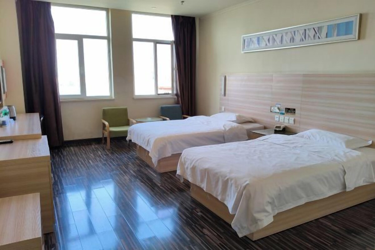 A hotel room with two beds, a desk, a chair, and a window with curtains.
