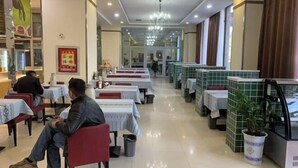 A restaurant with tables and chairs, a chandelier, and a tiled wall.