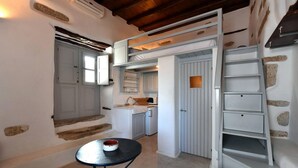 A compact kitchen with a built-in oven, a sink, and a small dining area with a table and chairs. - Kastro Cozy Guesthouse (Paros)
