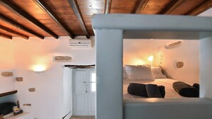 A cozy bedroom with a bed, pillows, and a nightstand. There is a wooden ceiling and a stone wall. - Kastro Cozy Guesthouse (Paros)