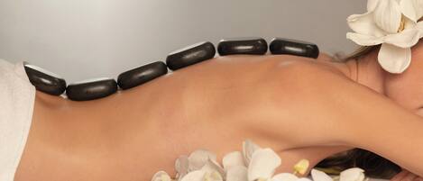 A person receiving a massage with stones and white flowers on a white surface.