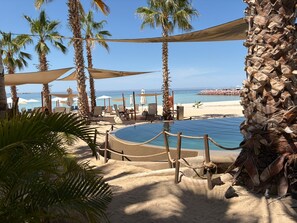 A poolside area with lounge chairs, palm trees, and a view of the beach and ocean. - Condo Cortes  (La Paz)