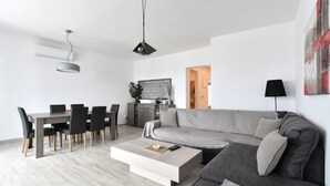 A modern living room with a grey sofa, a dining table with chairs, and a coffee table. - Parikia s Seaside House (Paros)
