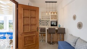 A modern kitchen with a wooden door, bar stools, and a blue sofa. - Theodora s Suite in Agios Charalampos (Paros)