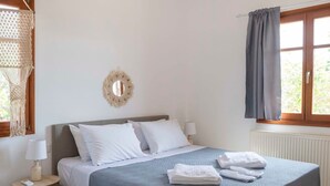 A neatly arranged bedroom with a bed, bedside table, lamp, and a hanging light fixture. - Theodora s Suite in Agios Charalampos (Paros)